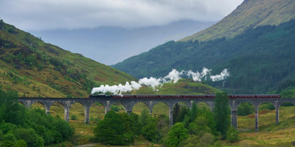 a train crossing a bridge over a river with a lush green hillside