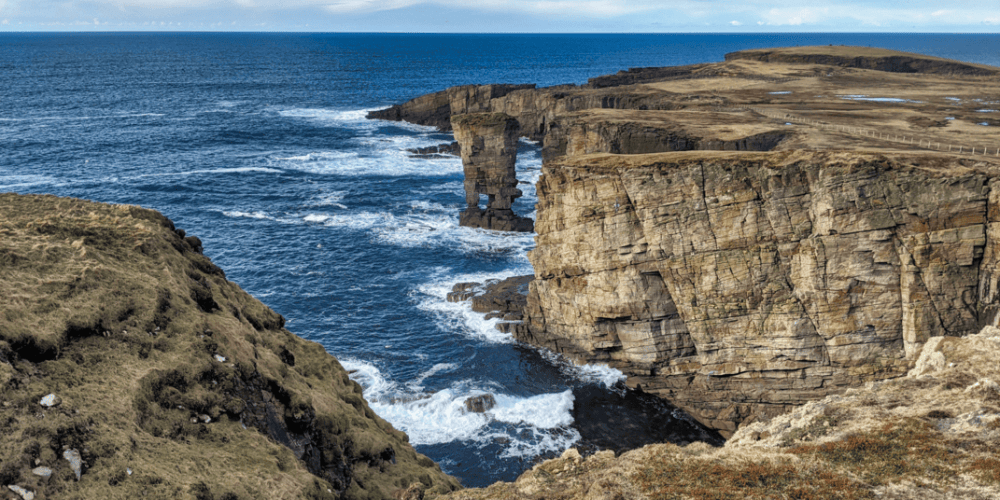 a close up of a rock near the ocean with Yesnaby in the background